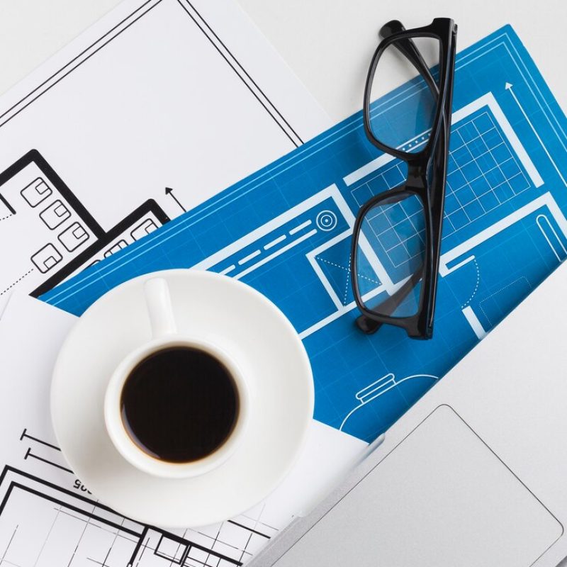 close-up-coffee-cup-with-blueprints-desk_23-2148397886